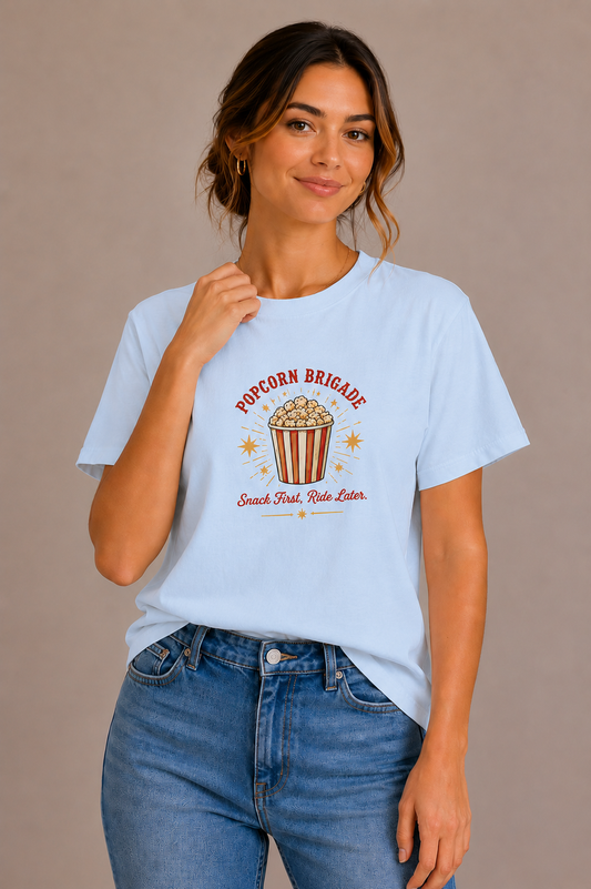 Woman wearing a blue crew-neck t-shirt with the 'Popcorn Brigade – Snack First, Ride Later' popcorn bucket design printed on the chest