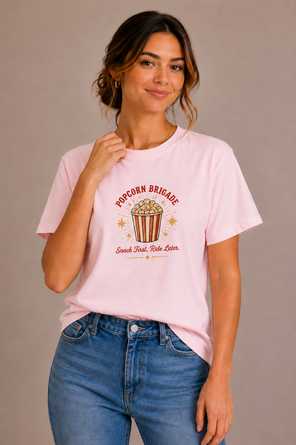 Woman wearing a pink crew-neck t-shirt with the 'Popcorn Brigade – Snack First, Ride Later' popcorn bucket design printed on the chest