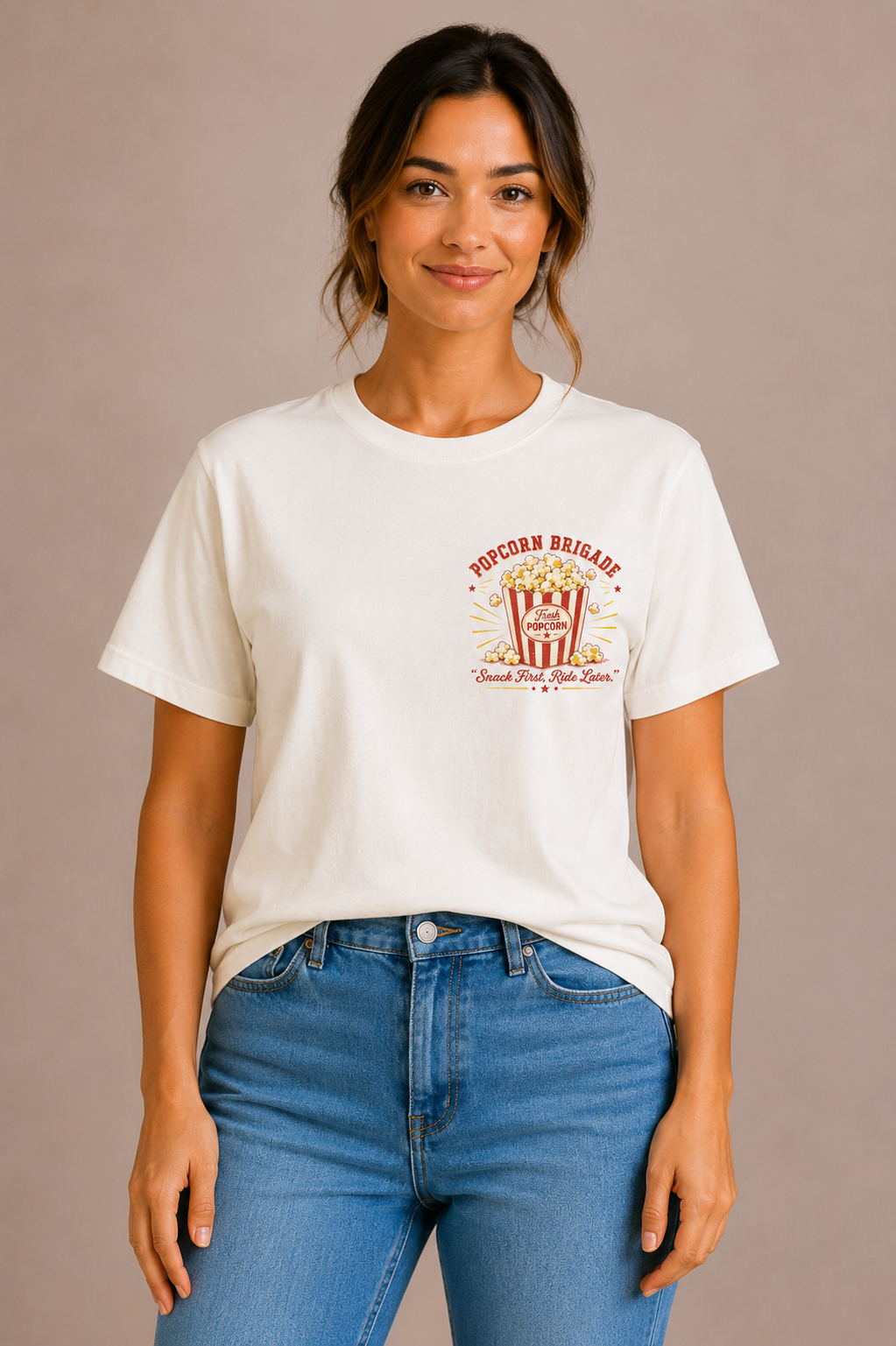 Woman wearing a sand crew-neck t-shirt with the 'Popcorn Brigade – Snack First, Ride Later' popcorn bucket design printed on the chest