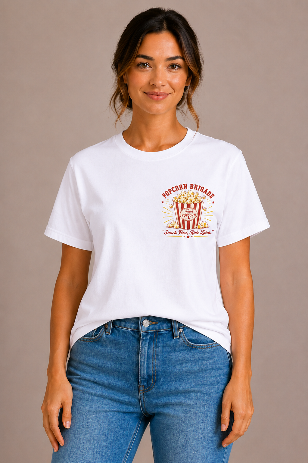 Woman wearing a white crew-neck t-shirt with the 'Popcorn Brigade – Snack First, Ride Later' popcorn bucket design printed on the chest
