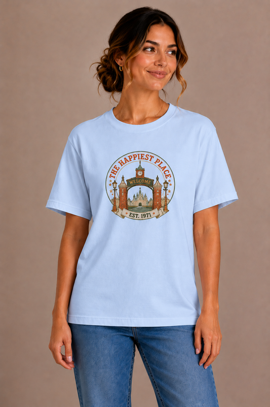 Woman wearing a blue crew-neck t-shirt with the 'The Happiest Place Est. 1971' castle gateway badge design printed on the chest