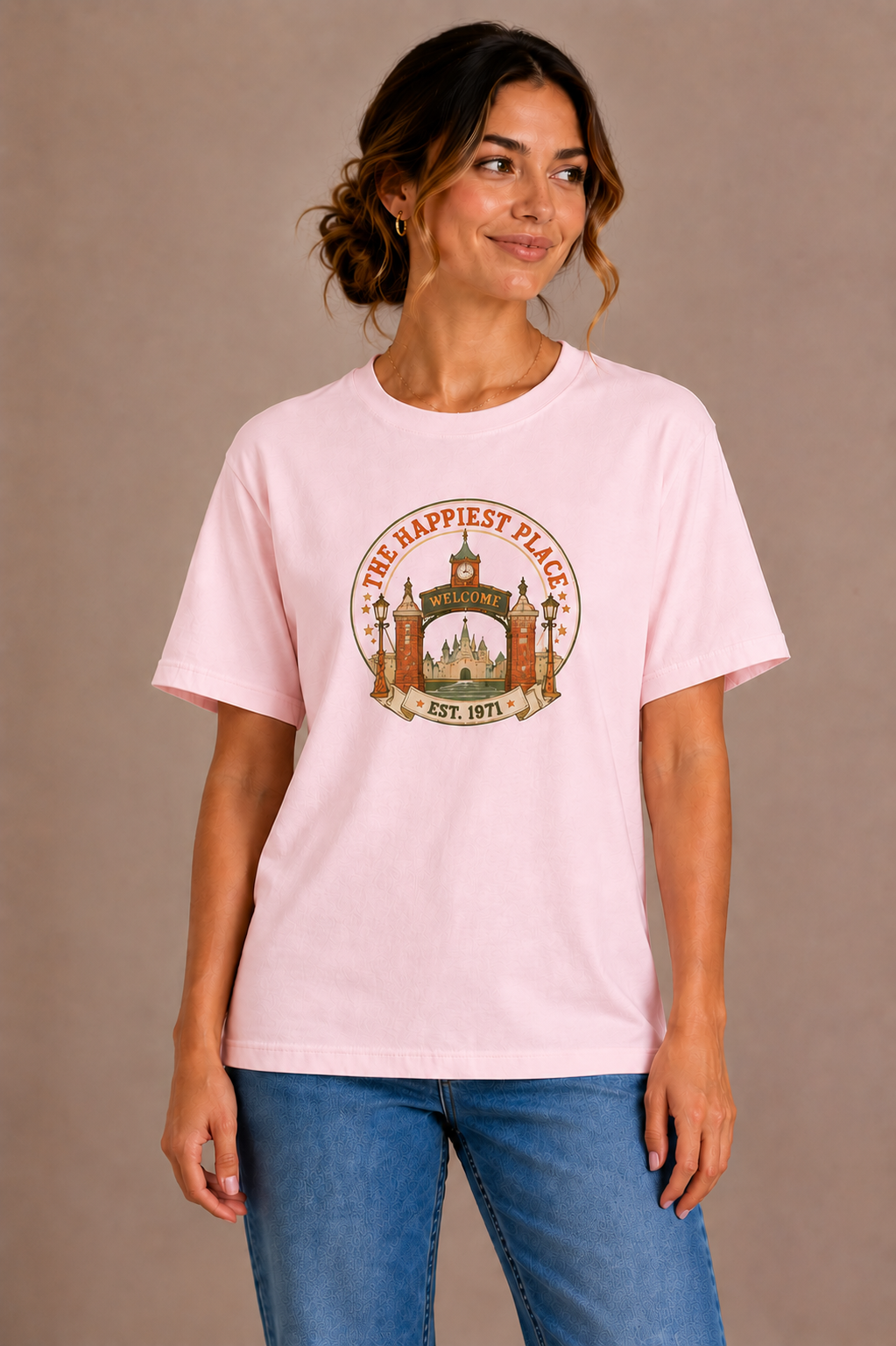 Woman wearing a pink crew-neck t-shirt with the 'The Happiest Place Est. 1971' castle gateway badge design printed on the chest