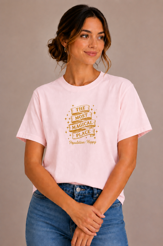 Woman wearing a pink crew-neck t-shirt with the 'The Most Magical Place – Population: Happy' ribbon banner design printed on the chest