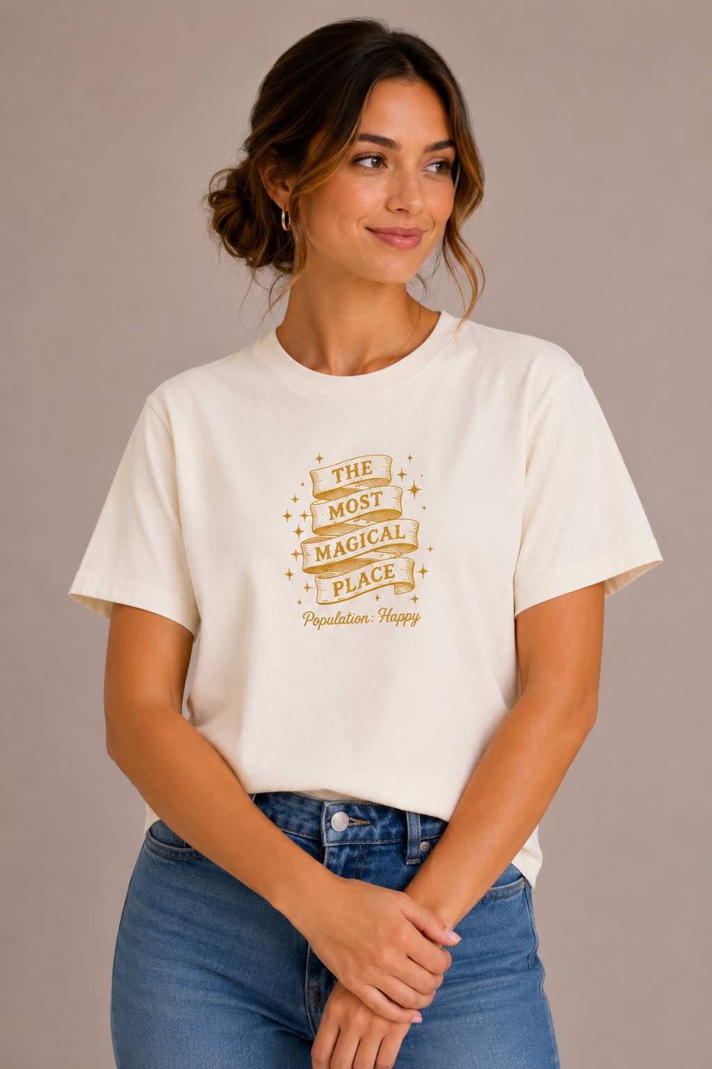 Woman wearing a sand crew-neck t-shirt with the 'The Most Magical Place – Population: Happy' ribbon banner design printed on the chest